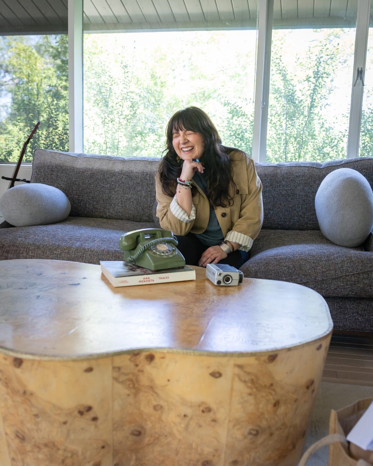 Frances laughing on a couch beside a rotary phone and a film camera