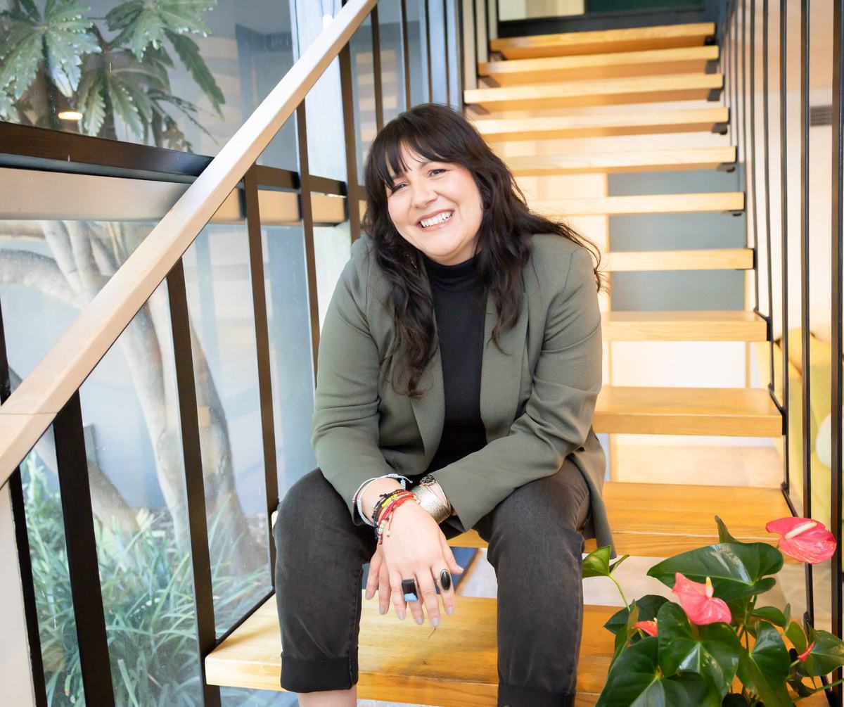 Frances Méndez smiling, seated on a wooden staircase