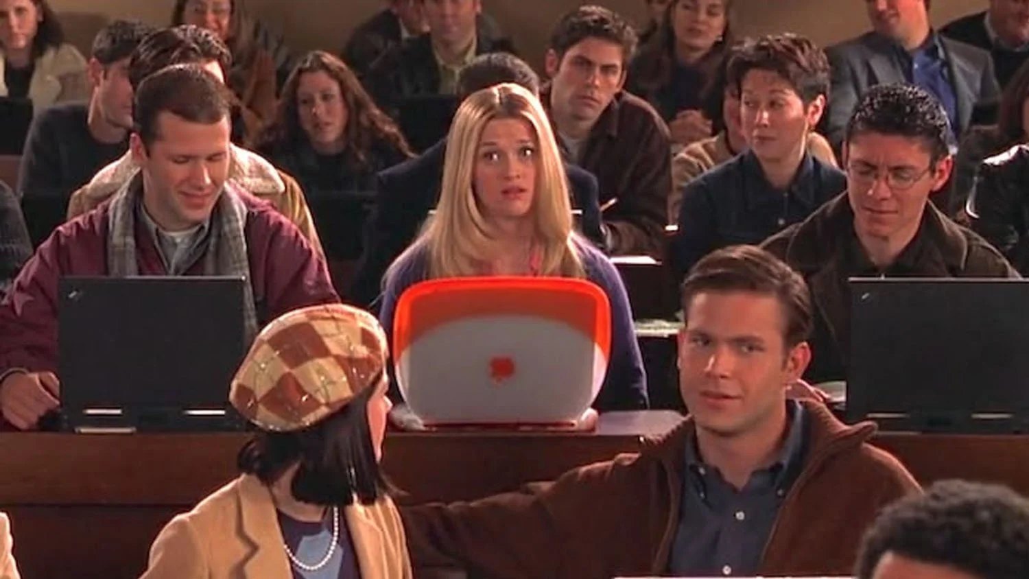 A lecture hall where every student is working on a laptop, and one woman in the middle row looks up from hers